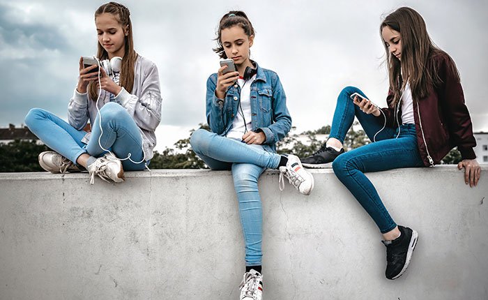 3 teenaged girls looking at their phones