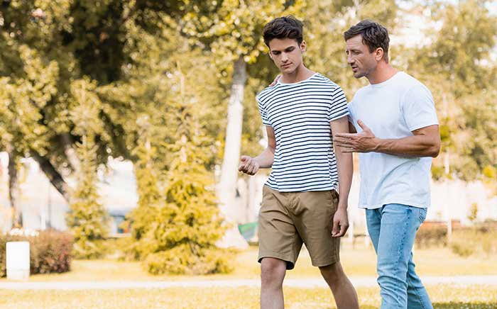 Father talks to teen son while walking in park