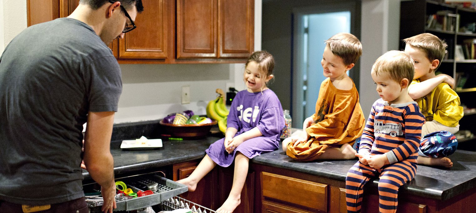 Young children watch father pack dishwasher