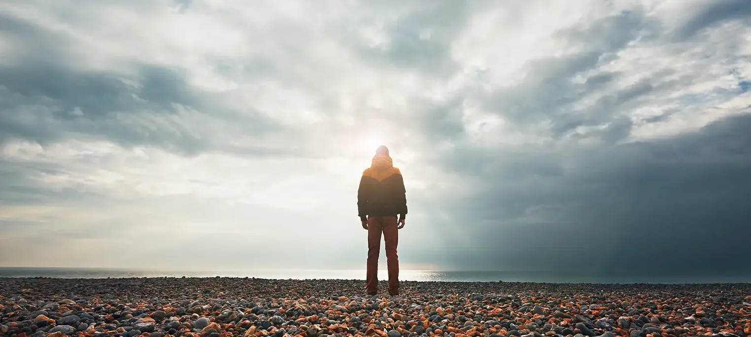 man blocks sun on pebble beach