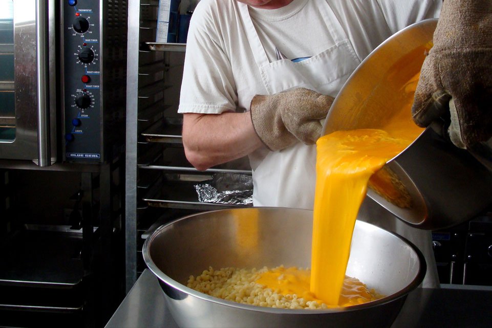 Kitchen worker pouring bulk sauce over pasta